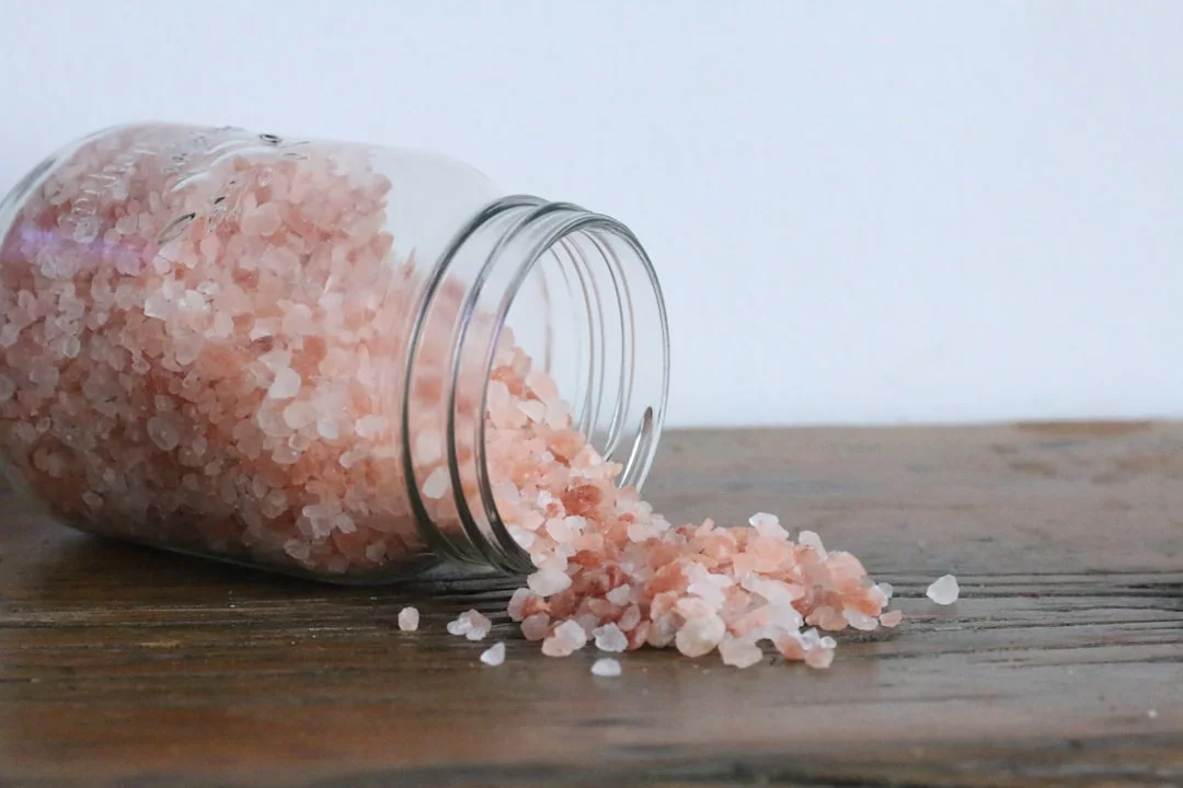 A wooden cutting board with a small ceramic salt cellar overflowing with large flaky sea salt crystals, a sliced steak resting nearby, and several open tins of specialty sea salts arranged in soft natural light
